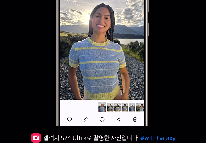 한 여성이 자갈밭에서 노을을 등지고 서서 카메라를 보며 환하게 웃고 있습니다. 역광임에도 여성의 모습을 또렷하게 확인할 수 있습니다.
